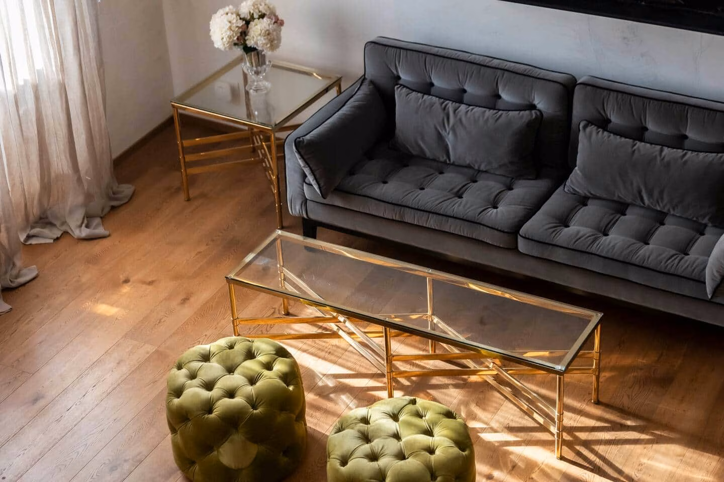 At Home — sitting area with a grey velvet tufted sofa, brass-and-glass coffee table and olive velvet ottomans