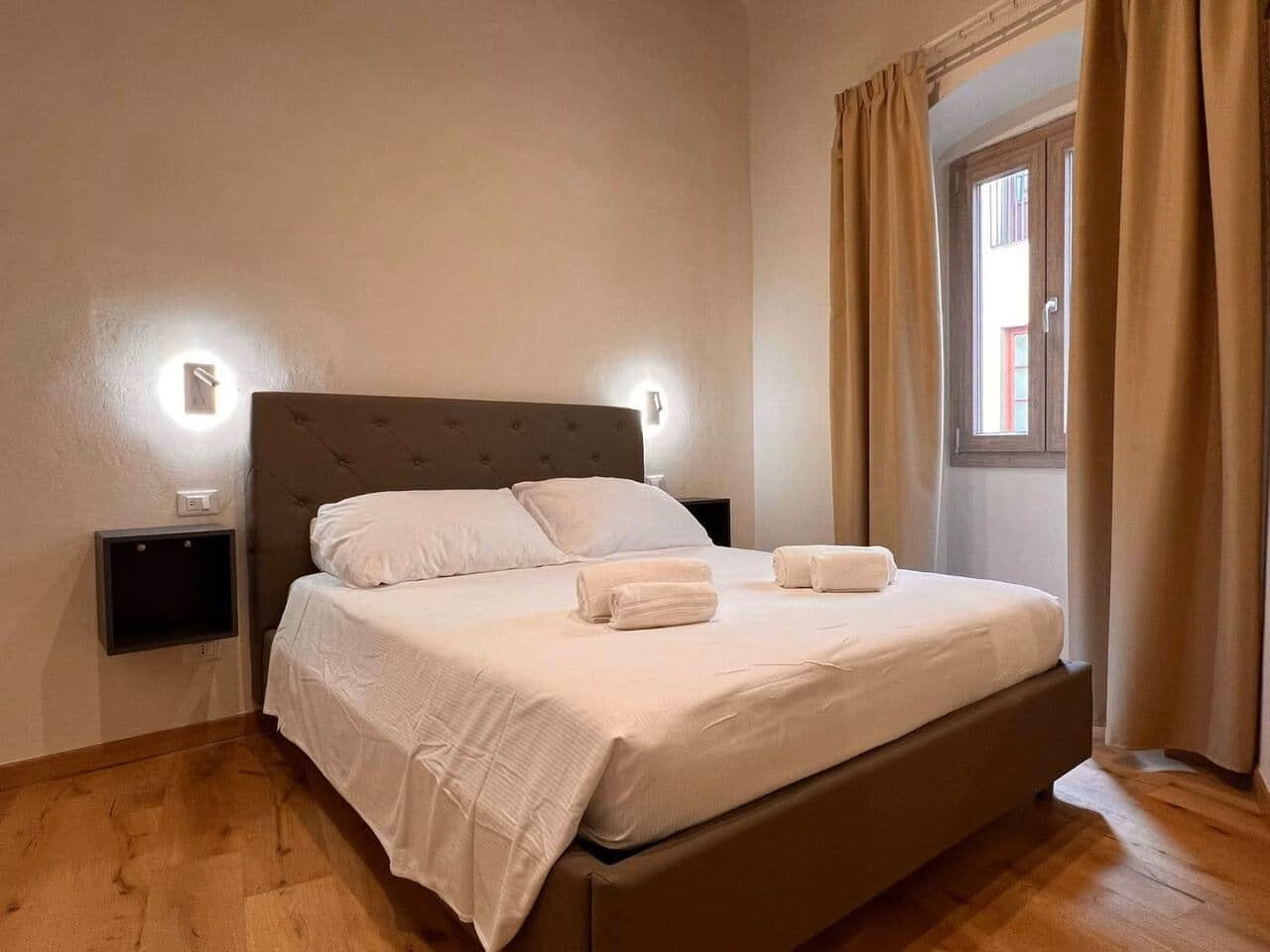 Sprone Left — second bedroom with an upholstered headboard and a curtained window over a Florentine facade